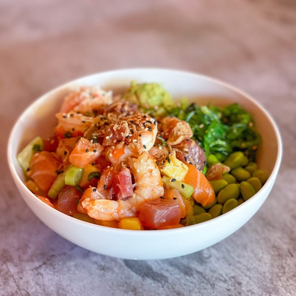 A vibrant Yo Poké Fusion bowl with shrimp, salmon, tuna, edamame, seaweed salad, and avocado.