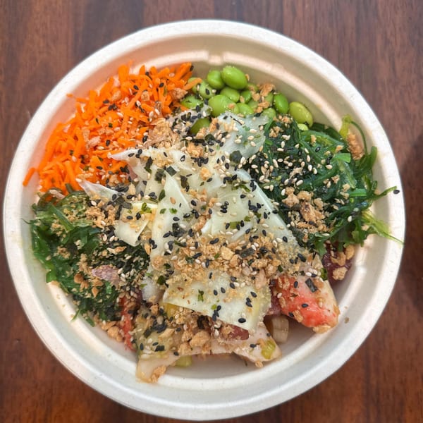Colorful Yo Poké Fusion bowl with shredded carrots, edamame, seaweed, and crab, topped with sesame seeds.